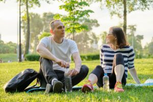 Middle-aged couple sitting on yoga mat, man and woman talking relaxing drinking water