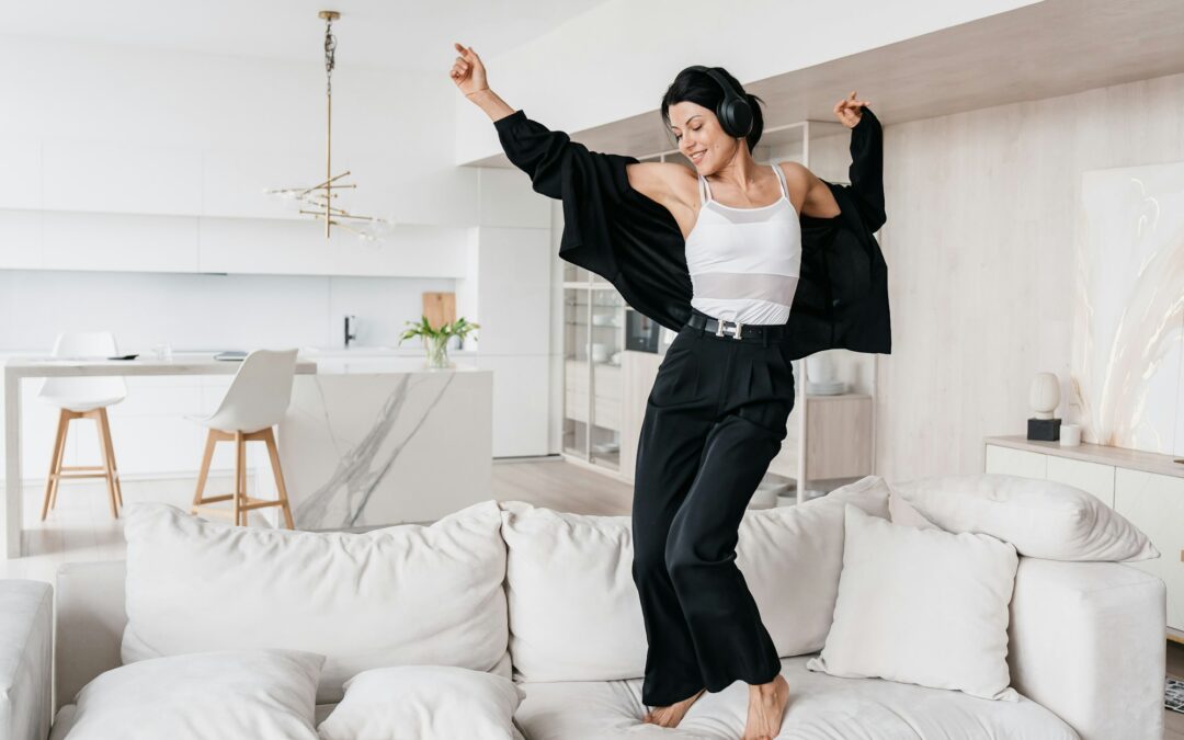 Young hispanic woman in black sweater and pants dancing on couch listening music using headphones